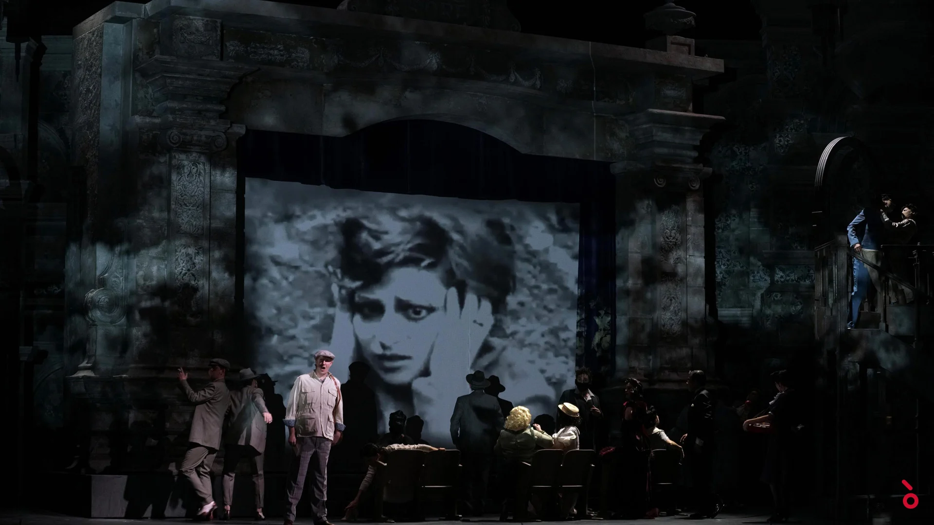 Black-and-white film close-up of a woman projected in the cinema arch above performers in period dress – Luisa Fernanda at Teatro de la Zarzuela, Madrid, Spain, 2021 – opera set design