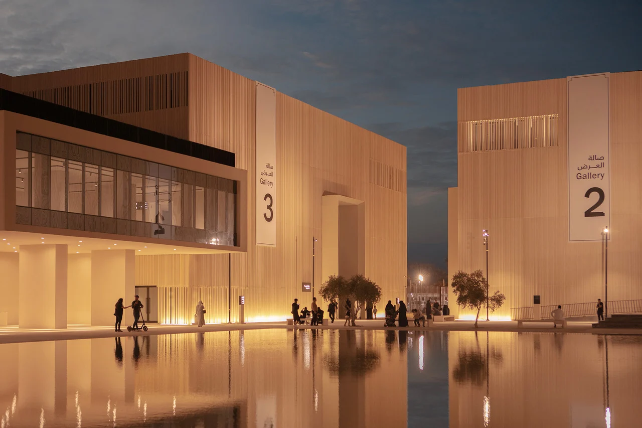 Galleries 2 and 3 lit at night, visitors walking along the reflecting pool between the pavilions – Islamic Arts Biennale, Jeddah, Saudi Arabia, 2023 – architecture