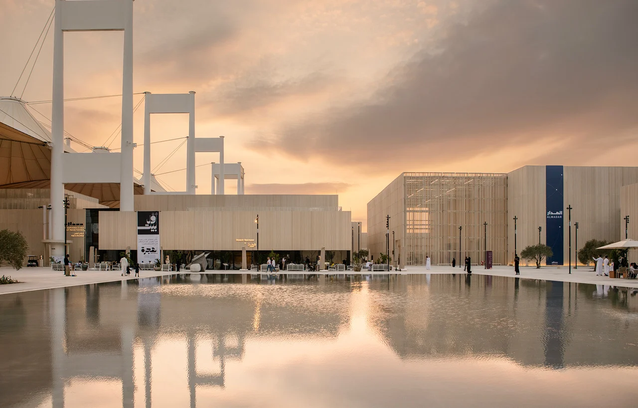 Biennale pavilions at sunset beside the white tent pylons of the Hajj Terminal, mirrored in a reflecting pool – Islamic Arts Biennale, Jeddah, Saudi Arabia, 2023 – architecture