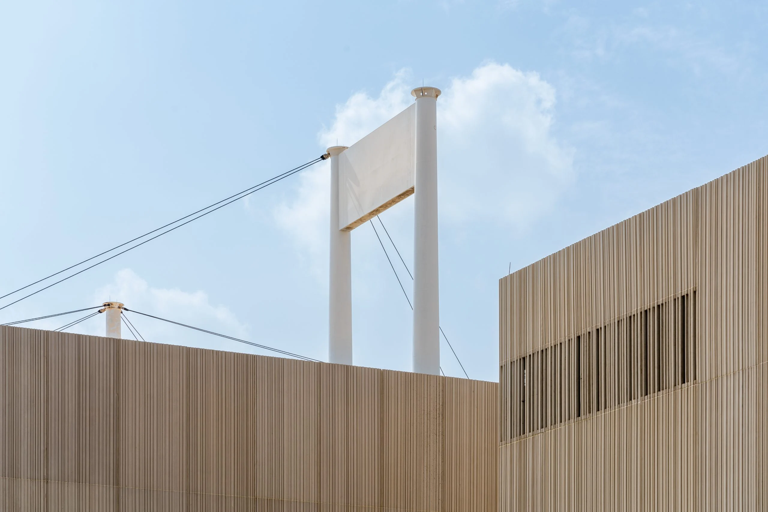 Slatted pavilion walls against the sky, with a white tent pylon and its cables rising behind – Islamic Arts Biennale, Jeddah, Saudi Arabia, 2023 – architecture