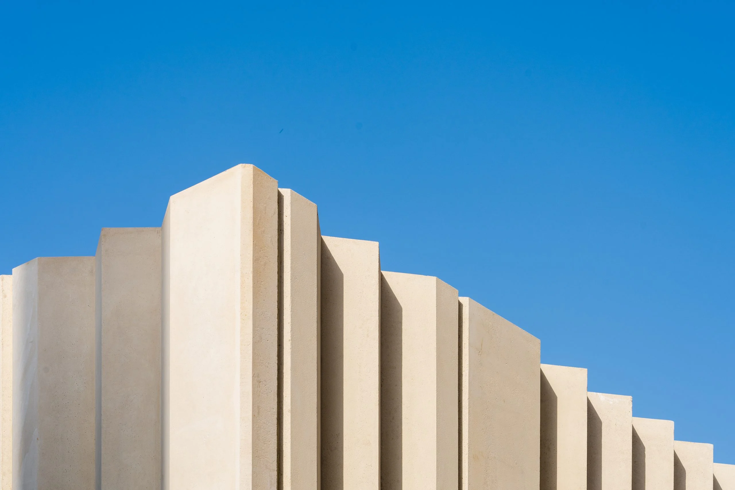 Stepped beige fins of a pavilion wall cutting into a deep blue sky – Islamic Arts Biennale, Jeddah, Saudi Arabia, 2023 – architecture