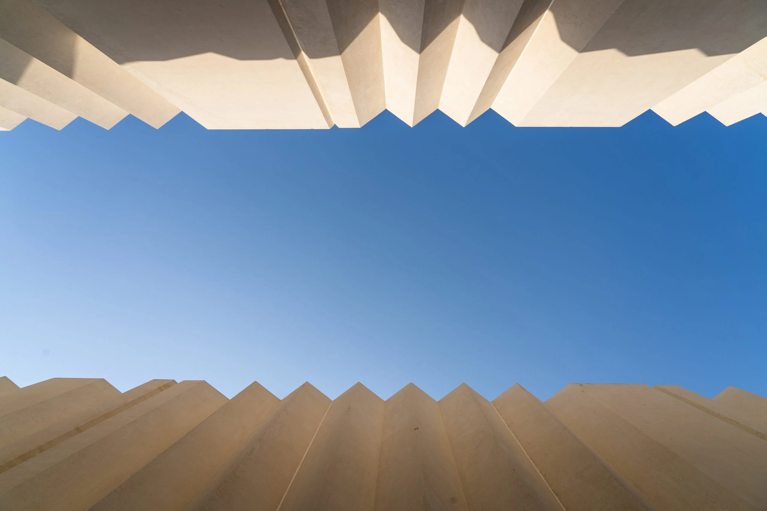 Upward view of blue sky framed by the zigzag edges of two folded pale walls – Islamic Arts Biennale, Jeddah, Saudi Arabia, 2023 – architecture