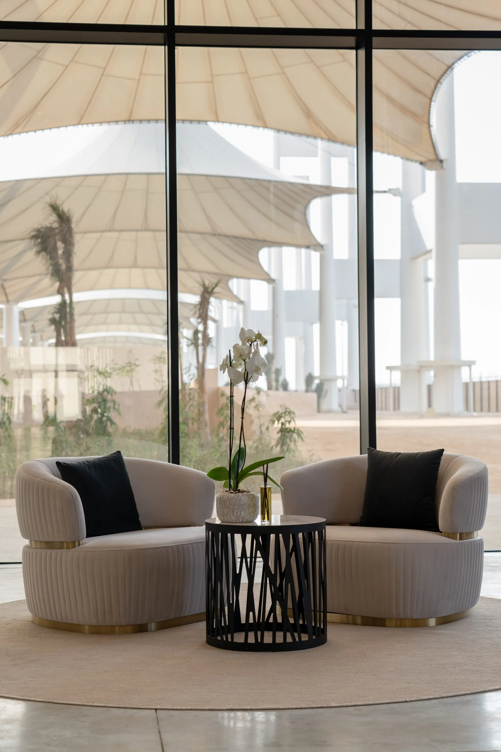 Lounge with two curved armchairs and an orchid before a glass wall overlooking the white tent canopies – Islamic Arts Biennale, Jeddah, Saudi Arabia, 2023 – architecture