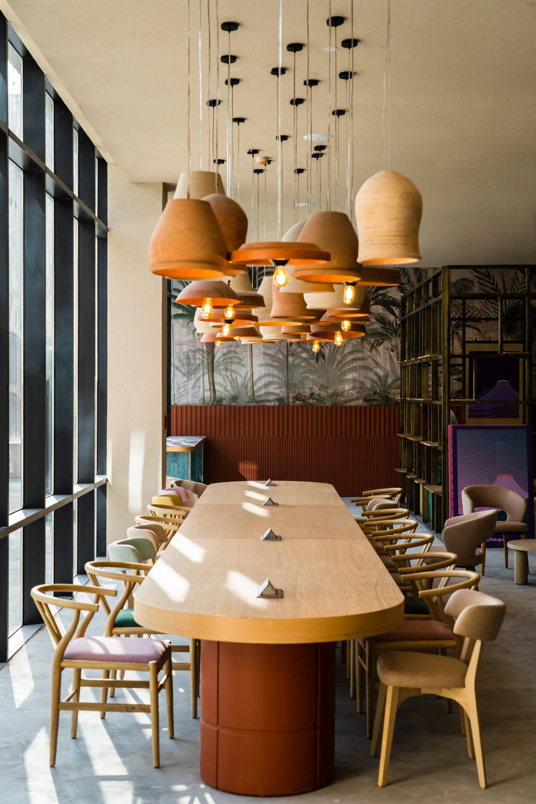 Long wooden communal table under clusters of terracotta pendant lamps, beside floor-to-ceiling windows – Islamic Arts Biennale, Jeddah, Saudi Arabia, 2023 – architecture