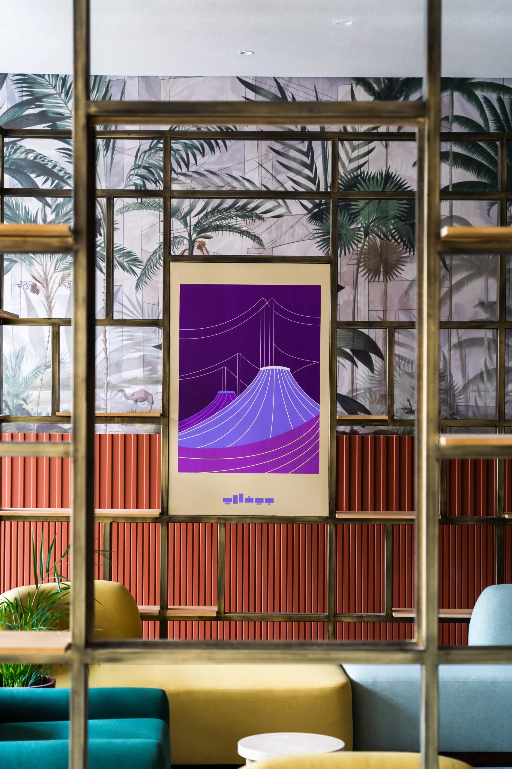 Purple poster of the Hajj Terminal tents framed in brass shelving against palm-print wallpaper – Islamic Arts Biennale, Jeddah, Saudi Arabia, 2023 – architecture
