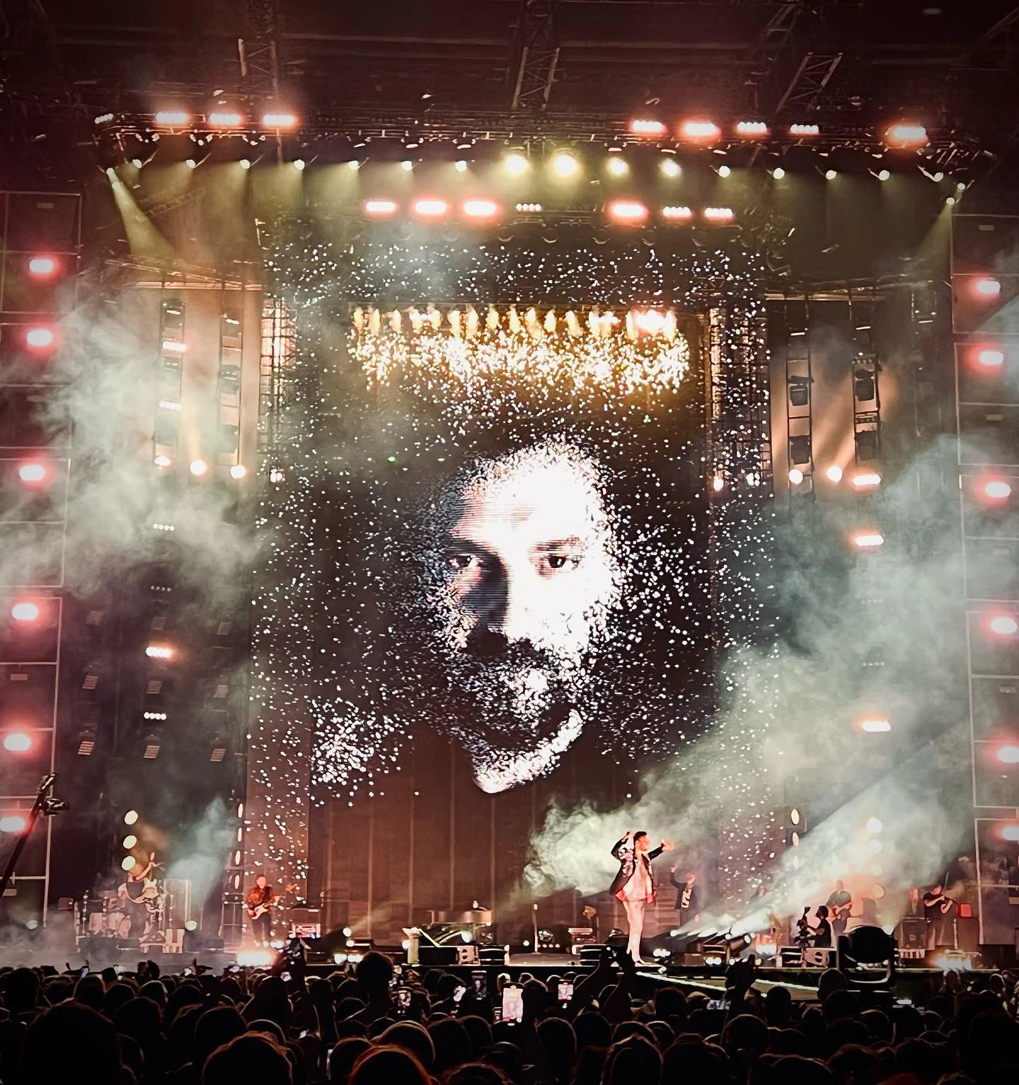 Giant LED wall showing the singer's face in sparkling particles, smoke and the band on stage below – Cesare Cremonini Stadi 2022, Italy – concert stage design