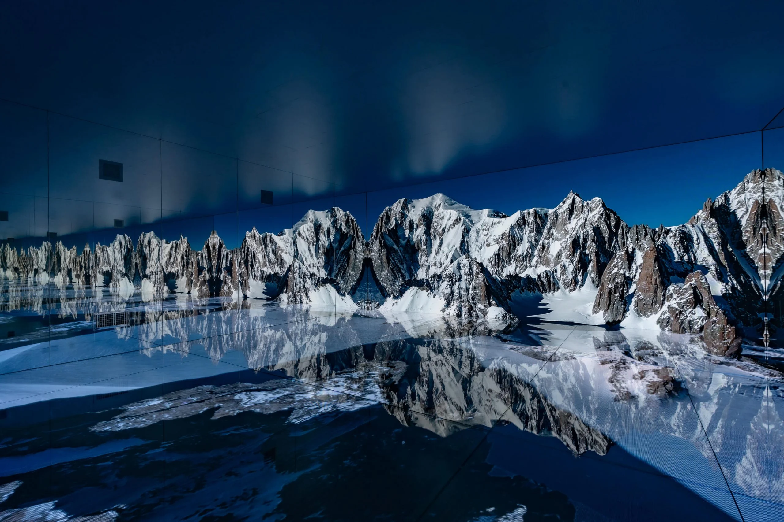 Panorama of the Mont Blanc massif on the LED wall, its peaks reflected across the dark mirrored floor – Mont Blanc Infinity Room at Skyway, Courmayeur, Italy, 2023 – installation design
