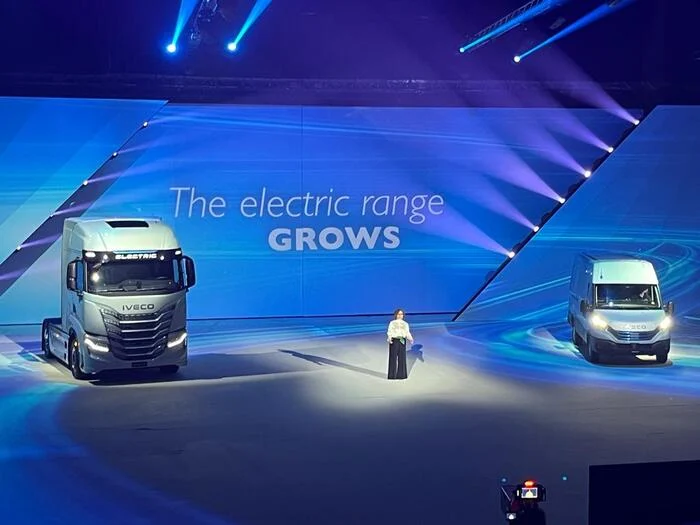 Presenter between an electric truck and a van, the screen reading The electric range grows – IVECO Be The Change Launch, Barcelona, Spain, 2023 – event design
