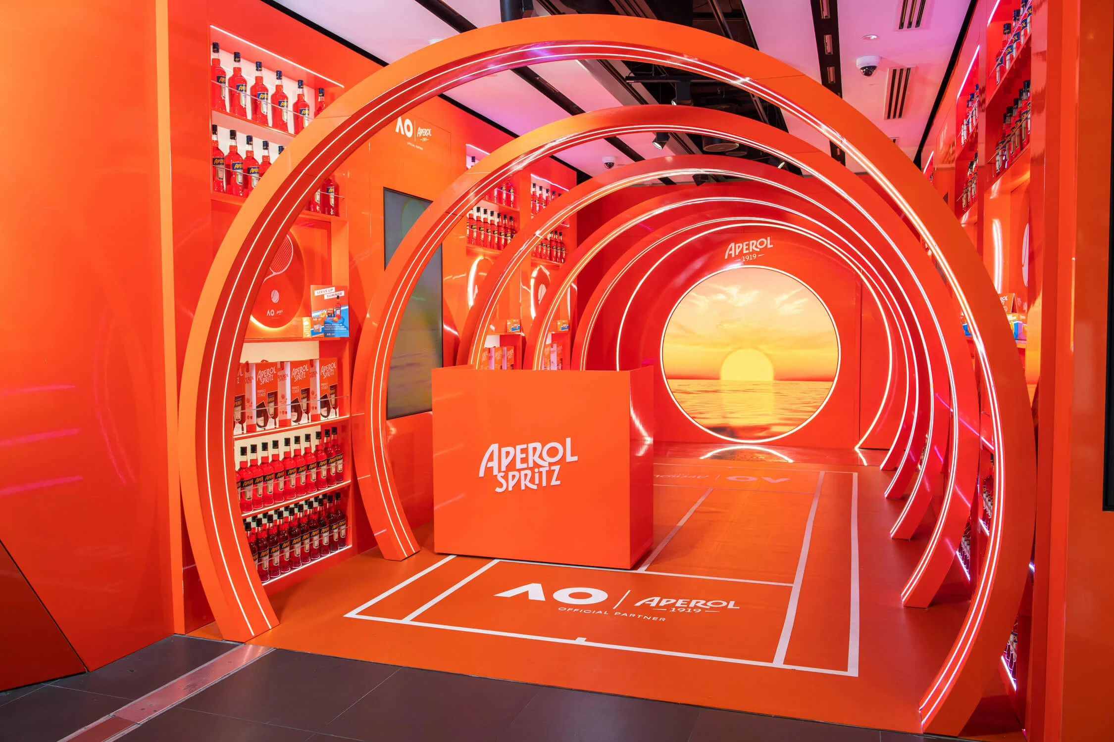 Angled view of the empty orange arch tunnel with the Aperol Spritz counter and court markings – Aperol Pop-Up at Melbourne Airport, Australia, 2024 – retail design