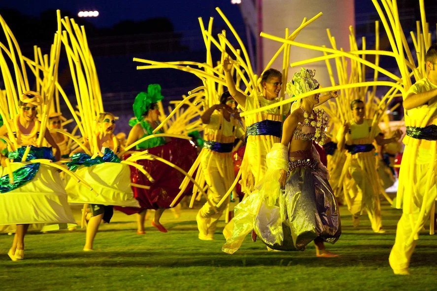 Performers in yellow costumes with tall flexible yellow rods dancing on the grass – Pescara 2009 Mediterranean Games Opening Ceremony, Italy, 2019 – event design