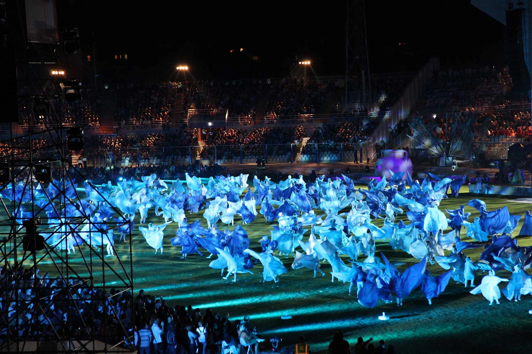 Hundreds of performers in flowing blue and white costumes covering the stadium field – Pescara 2009 Mediterranean Games Opening Ceremony, Italy, 2019 – event design