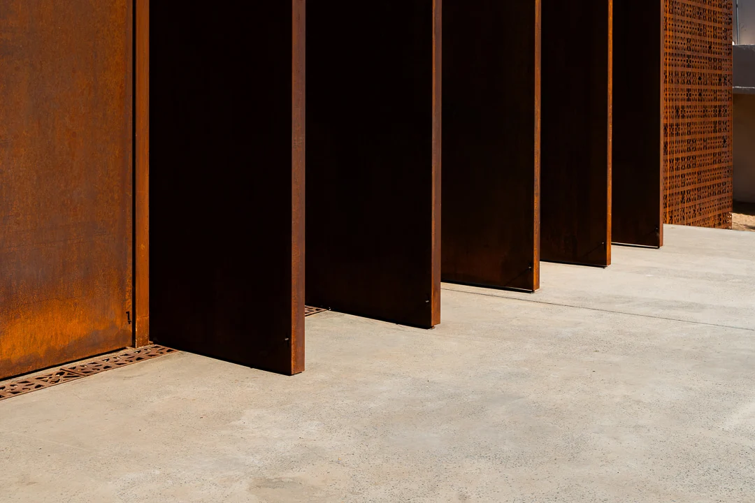 Detail of rust-coloured metal fins casting sharp shadows on a concrete floor – Design Space AlUla, Saudi Arabia, 2024 – architecture