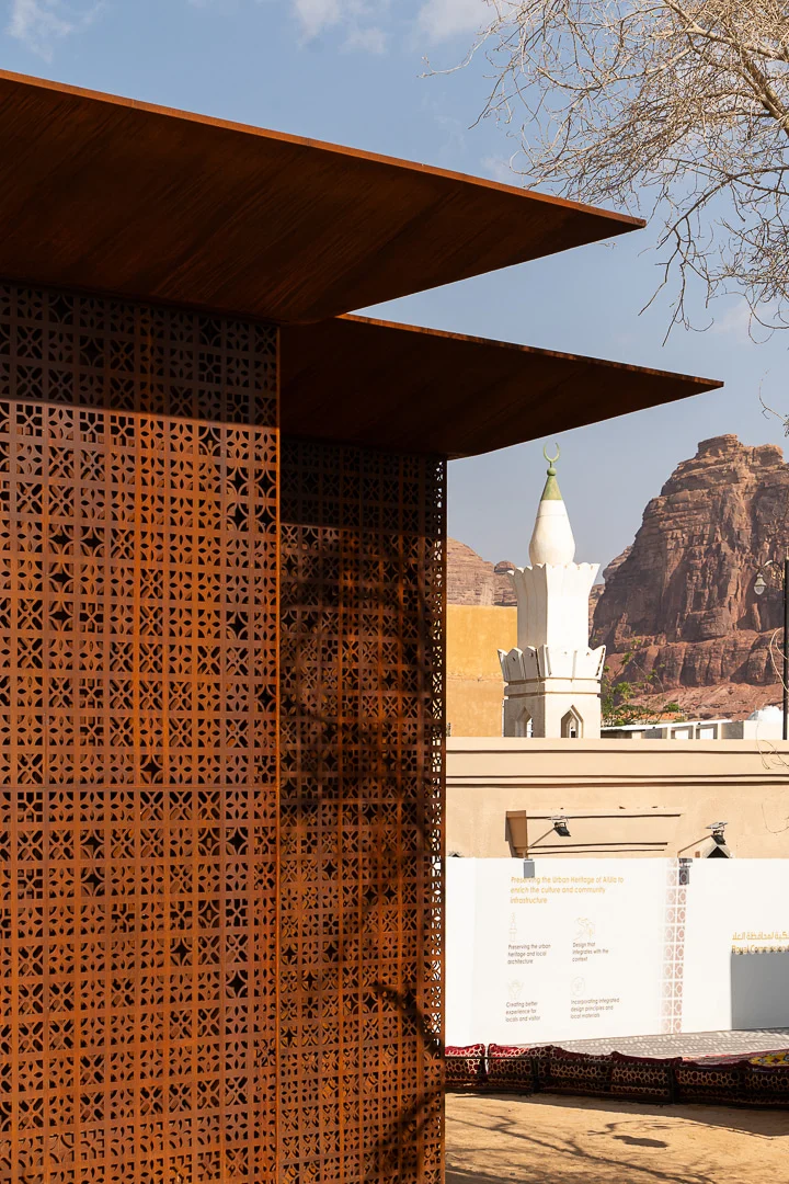 Corner of the perforated metal screen and roof overhang, a white minaret and red rock outcrops behind – Design Space AlUla, Saudi Arabia, 2024 – architecture
