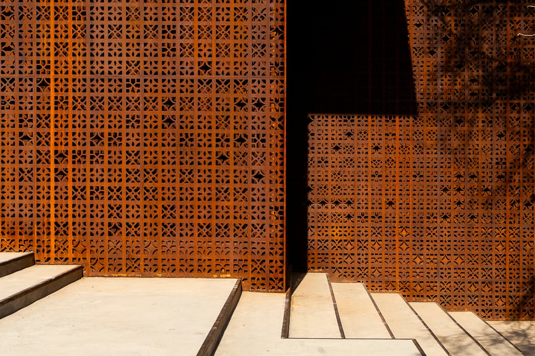 Close-up of the geometric perforated screen pattern above concrete steps, in sun and shade – Design Space AlUla, Saudi Arabia, 2024 – architecture