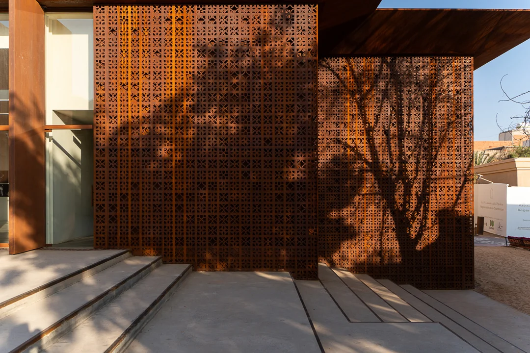Tree shadows cast on the rust-toned perforated metal screen above wide concrete steps – Design Space AlUla, Saudi Arabia, 2024 – architecture