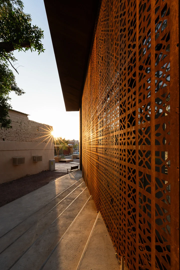 Low sun shining along the rust-toned perforated metal screen and stepped concrete paving – Design Space AlUla, Saudi Arabia, 2024 – architecture