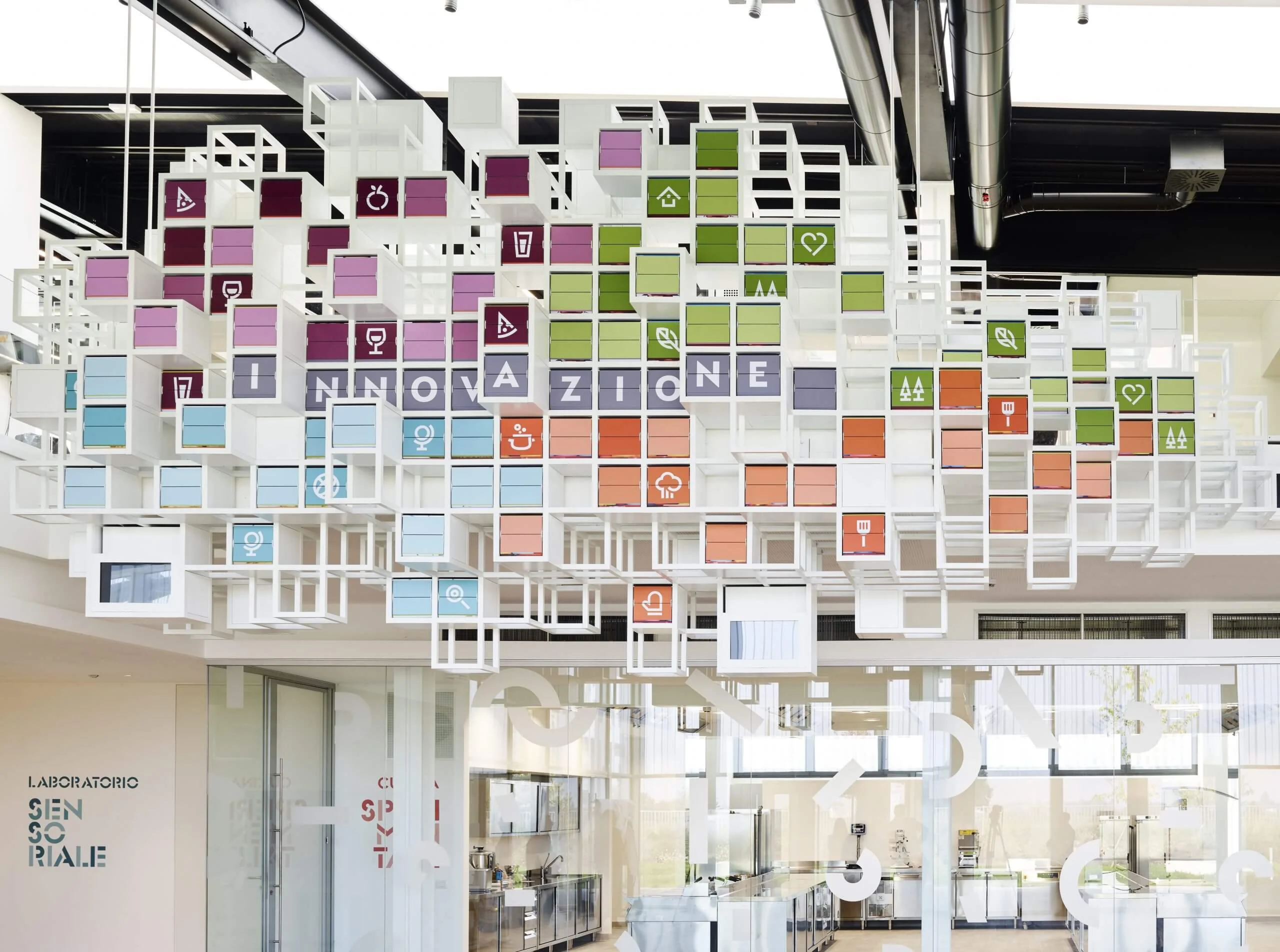 La Nuvola seen from below: white frame cubes with coloured food icons and the word "Innovazione" – La Nuvola at Cirfood District, Reggio Emilia, Italy, 2022 – kinetic installation design