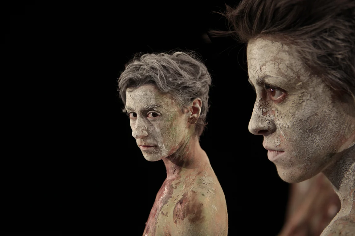 Close-up of two performers with cracked clay body paint, one in profile, against a black background – I Shardana at Teatro Lirico di Cagliari, Italy, 2013 – opera set design