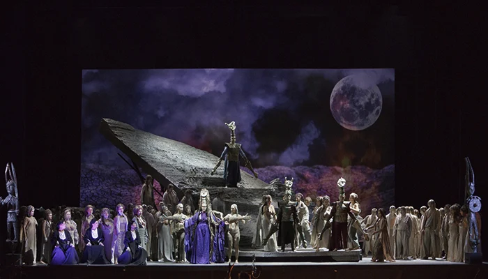 I Shardana staged at Teatro Lirico: chorus before a tilted stone slab under a projected moon – I Shardana at Teatro Lirico di Cagliari, Italy, 2013 – opera set design