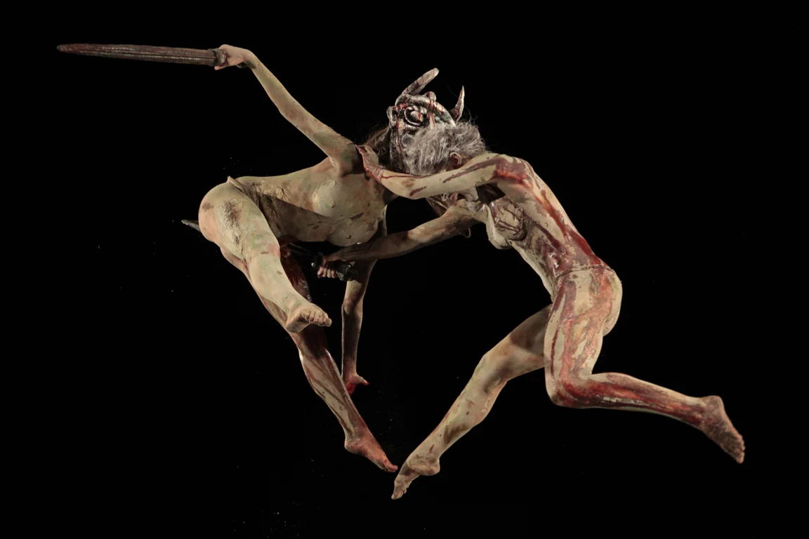 Two dancers covered in clay leap and fight in mid-air with swords against a black background – I Shardana at Teatro Lirico di Cagliari, Italy, 2013 – opera set design