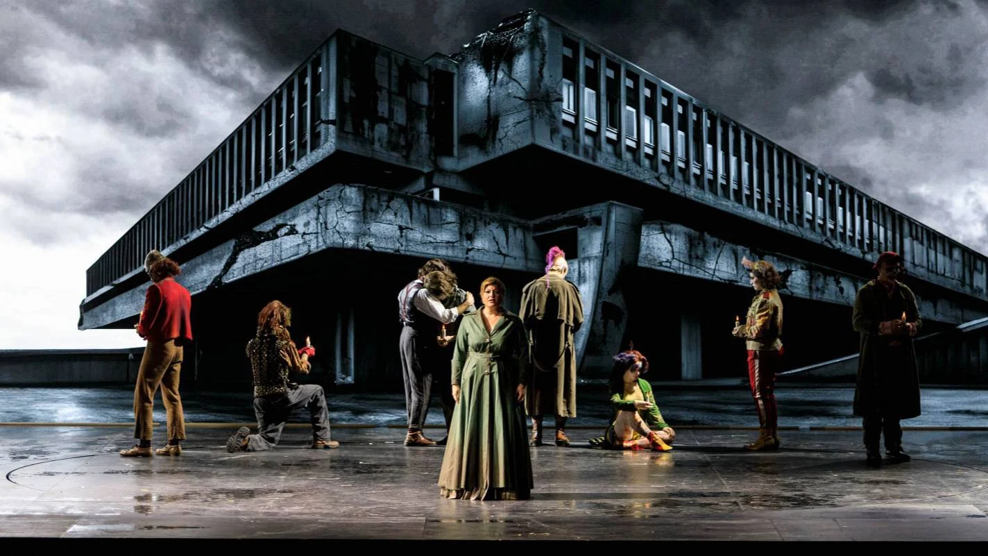Singers standing on a wet stage in front of a huge brutalist concrete building under a stormy sky – Il Trovatore at Teatro Comunale Nouveau, Bologna, Italy, 2024 – opera set design