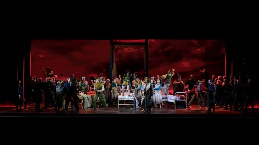 Chorus crowding a stage set with hospital beds before a blood-red sky backdrop – Il Trovatore at Teatro Comunale Nouveau, Bologna, Italy, 2024 – opera set design