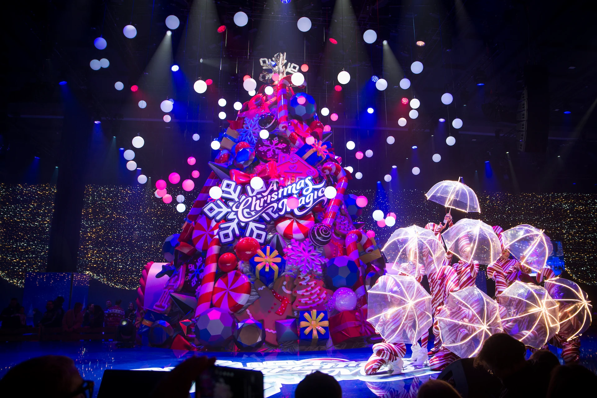 Dancers with glowing umbrellas beside the giant Christmas tree under hanging white light spheres – A Christmas Magic at Allianz MiCo, Milan, Italy, 2023 – event design
