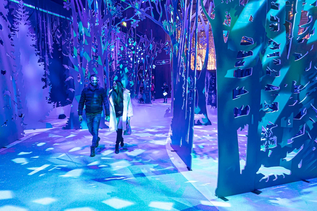 Visitors walking through a forest of cut-out tree panels lit in blue with snowflake projections – A Christmas Magic at Allianz MiCo, Milan, Italy, 2023 – event design