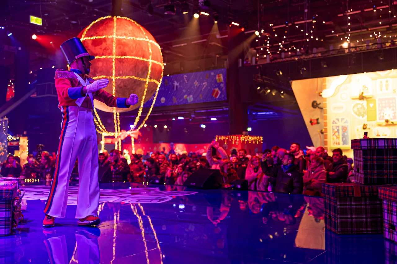 Performer in a top hat and toy-soldier costume on a reflective stage, a glowing balloon behind – A Christmas Magic at Allianz MiCo, Milan, Italy, 2023 – event design