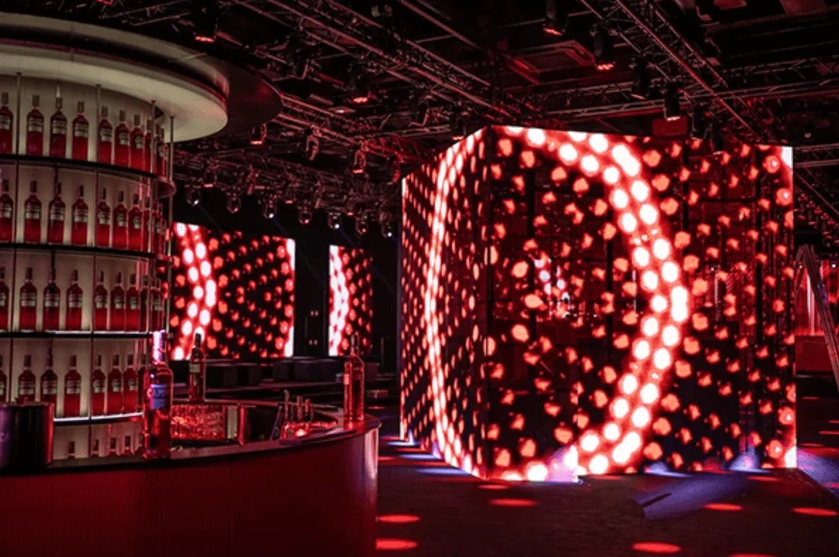 Curved bar with shelves of Campari bottles beside a large cube of red LED circles – Campari Discover Red Party at Cannes Film Festival, France, 2023 – event design
