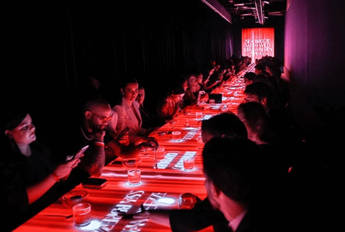 Guests at a long LED dinner table glowing red with projected text and drinks – Campari Discover Red Party at Cannes Film Festival, France, 2023 – event design