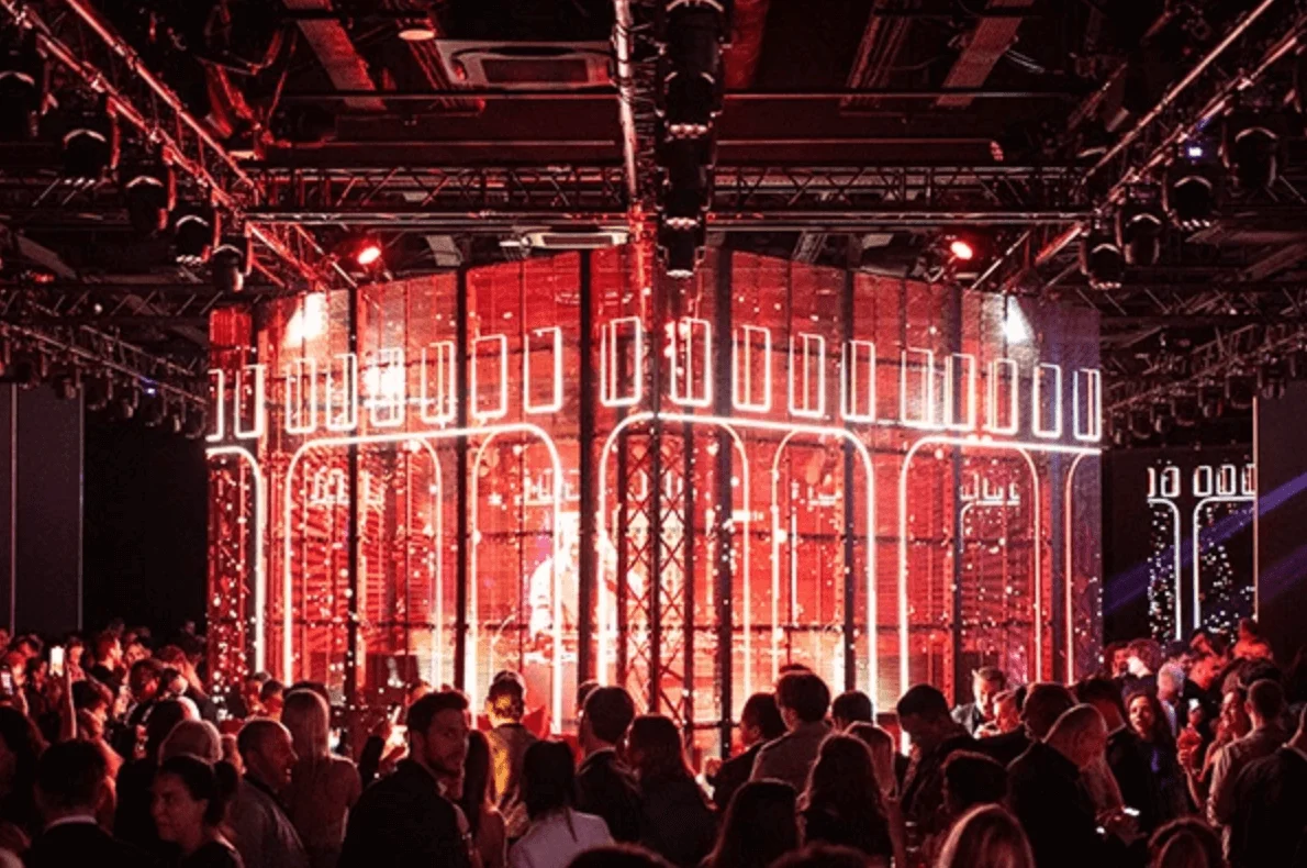 Crowd around a cylindrical red LED structure with white arch motifs under lighting trusses – Campari Discover Red Party at Cannes Film Festival, France, 2023 – event design