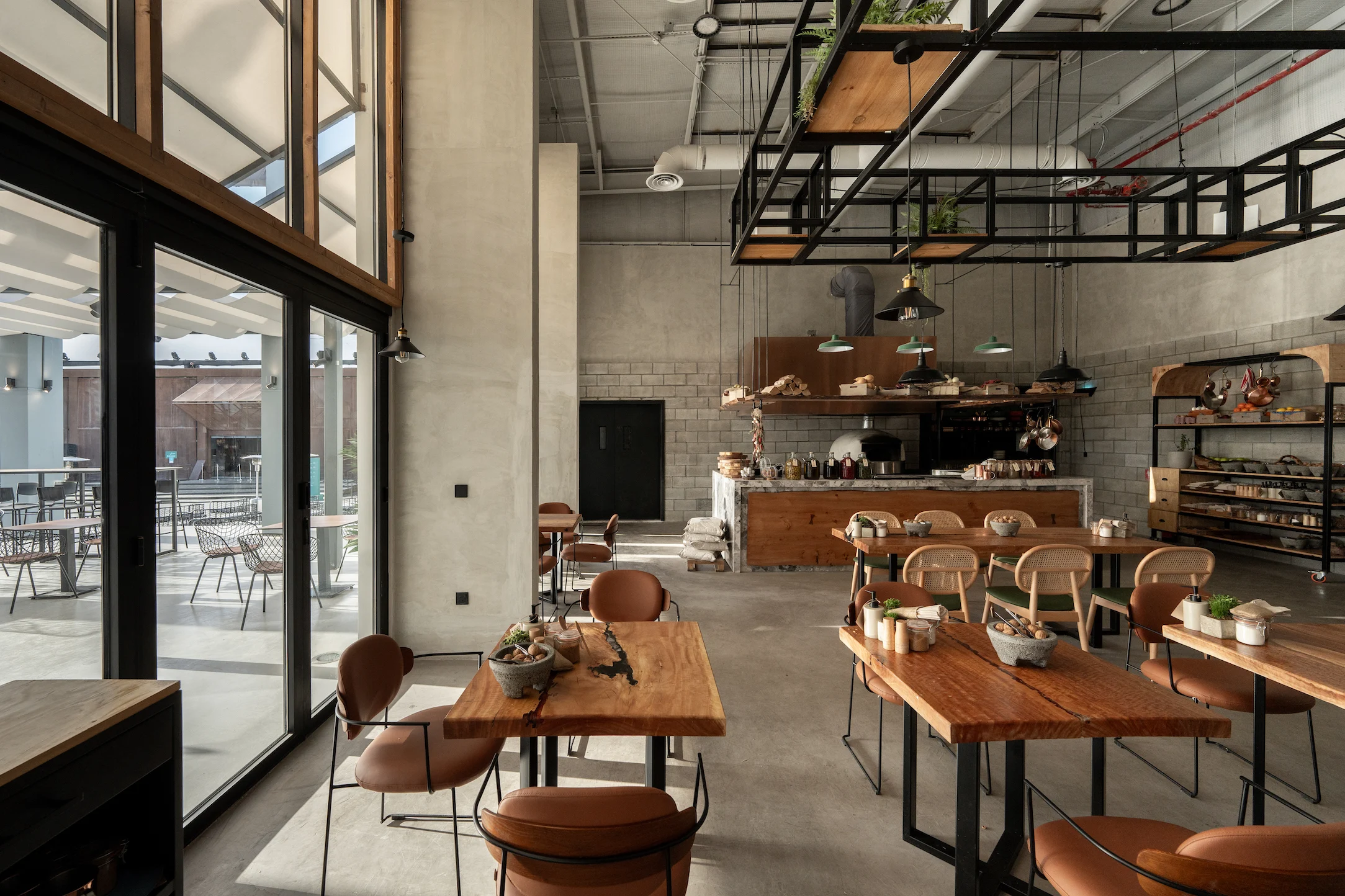 Bar interior with timber tables, tan leather chairs, concrete block walls and a black steel rack overhead – Diriyah Contemporary Art Biennale, Riyadh, Saudi Arabia, 2024 – architecture