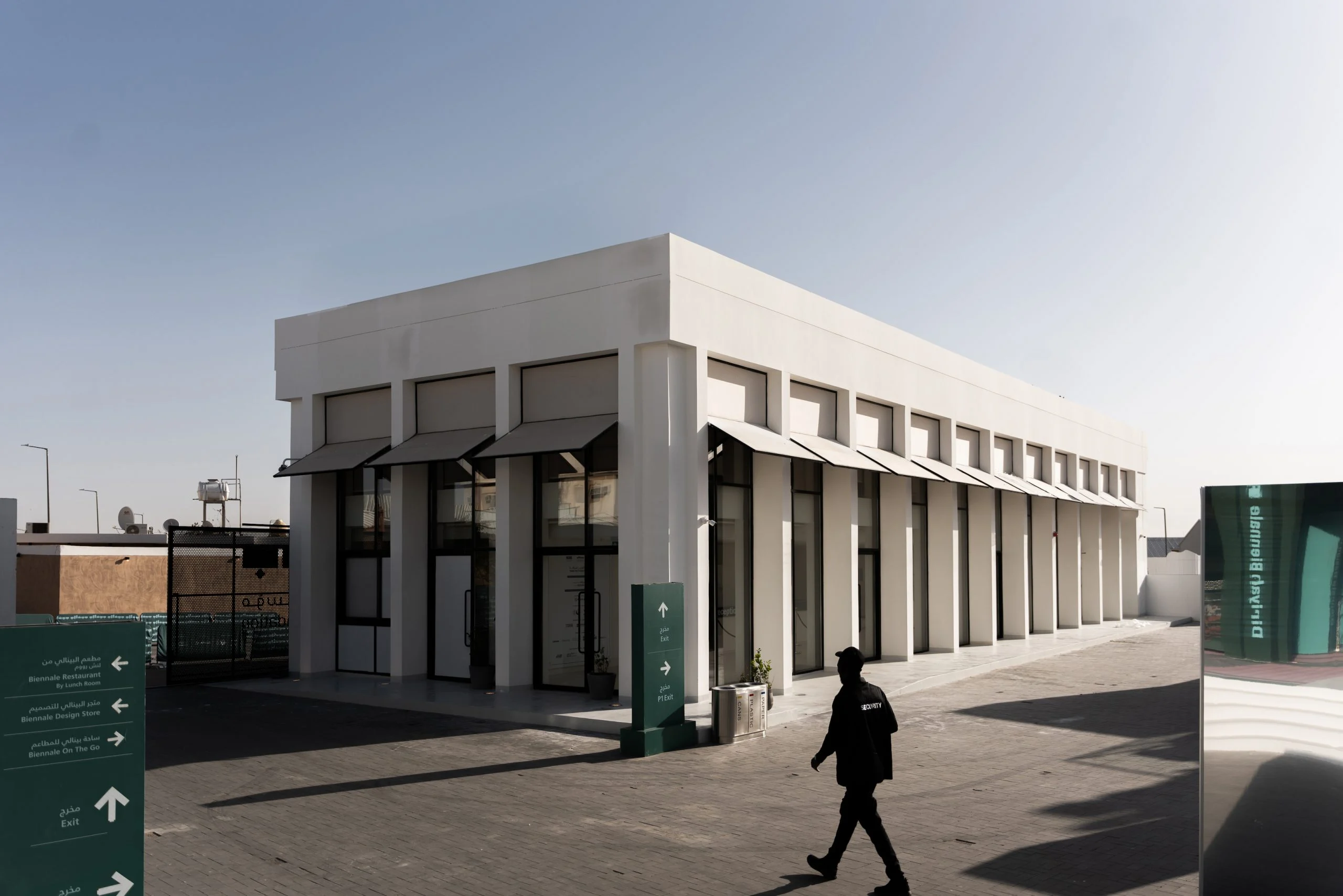 White reception building with slender piers and awnings, green wayfinding signs in the foreground – Diriyah Contemporary Art Biennale, Riyadh, Saudi Arabia, 2024 – architecture