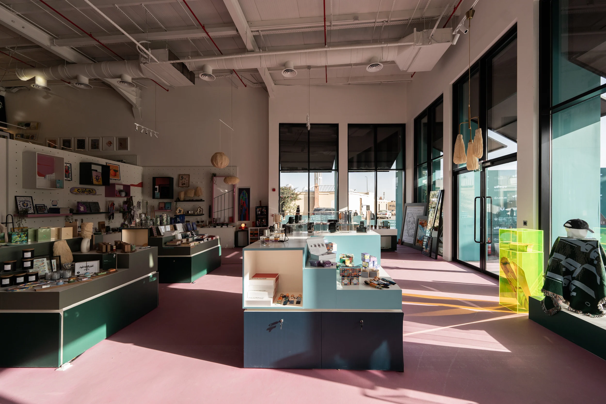 Design store interior with green and pale blue display tables, pink floor and tall windows – Diriyah Contemporary Art Biennale, Riyadh, Saudi Arabia, 2024 – architecture