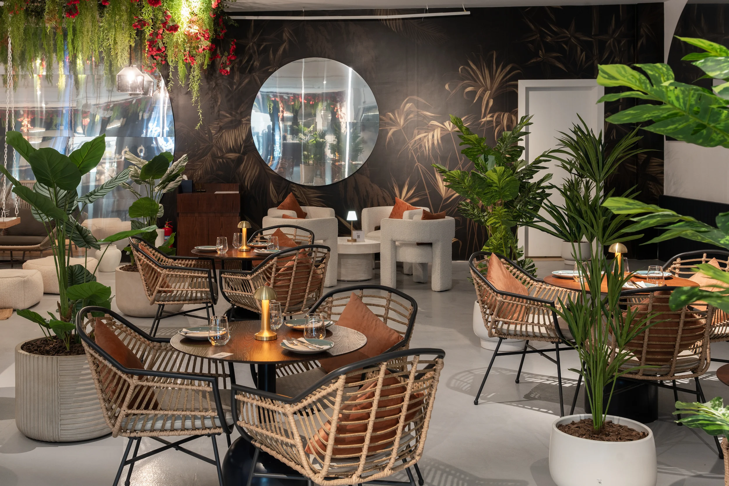 Restaurant with rattan chairs, potted palms, a round mirror and dark palm-leaf wallpaper – Diriyah Contemporary Art Biennale, Riyadh, Saudi Arabia, 2024 – architecture