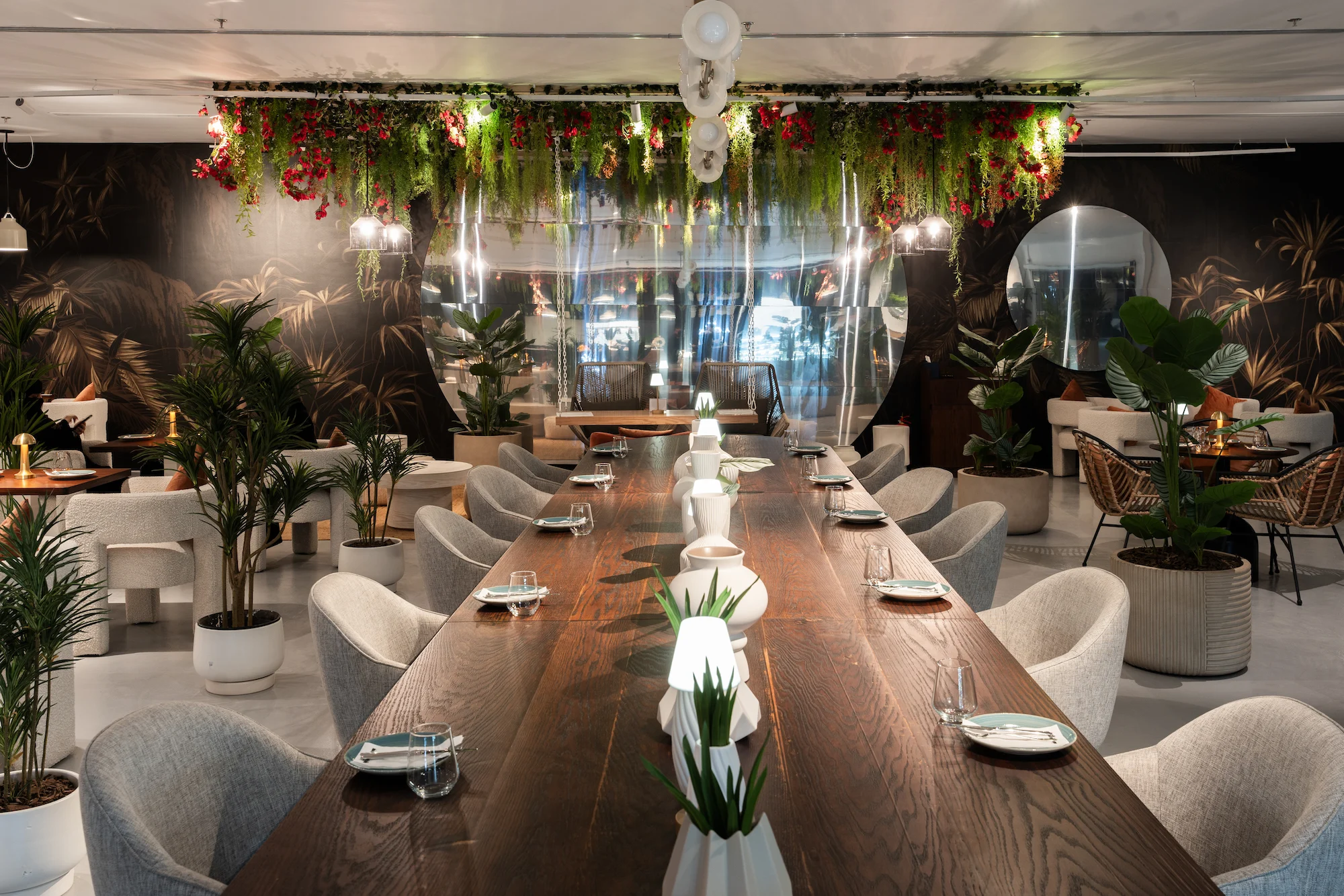 Long wooden communal table with grey upholstered chairs beneath a hanging garden of red flowers – Diriyah Contemporary Art Biennale, Riyadh, Saudi Arabia, 2024 – architecture