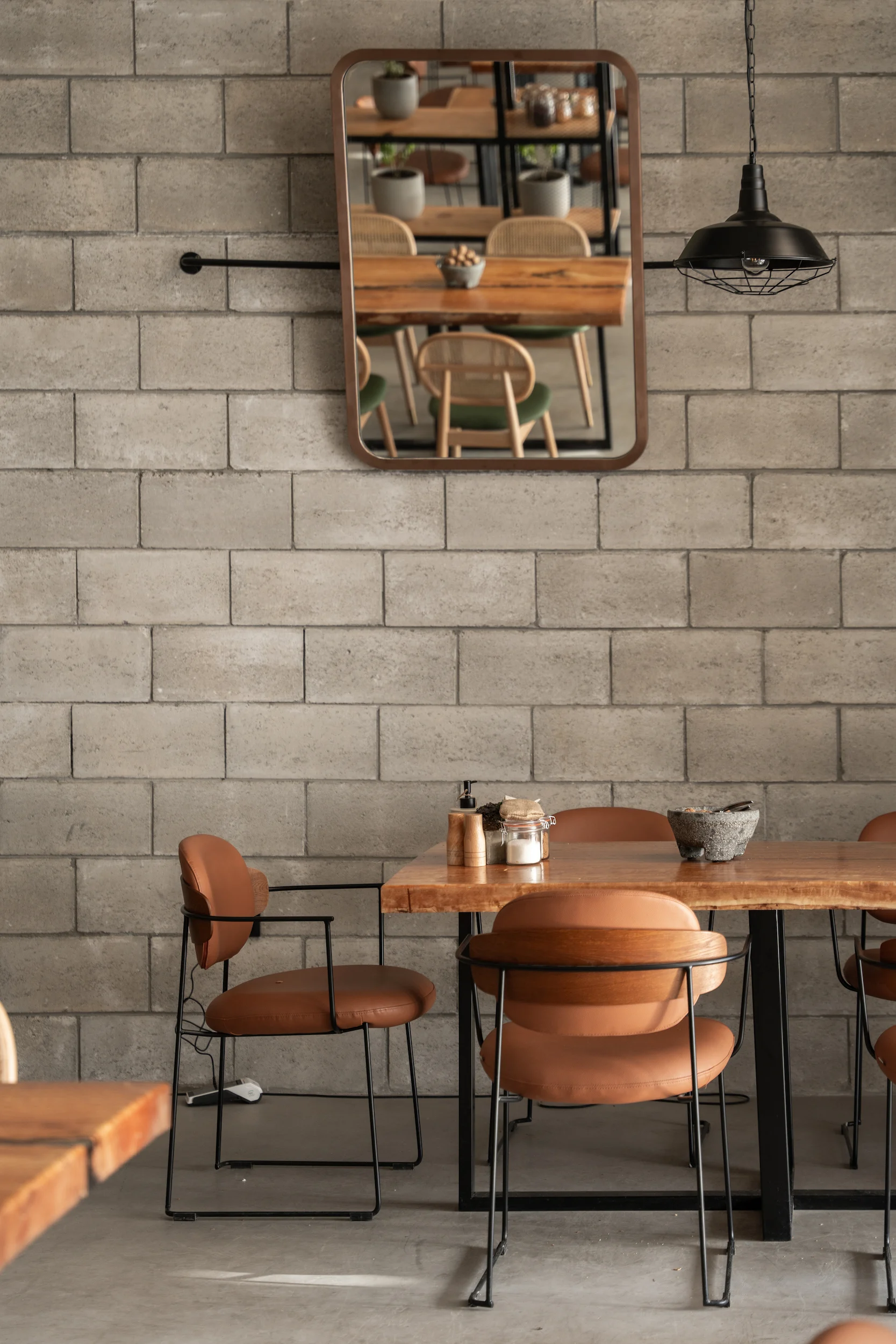 Tan leather chairs and wooden table against a concrete block wall with a mirror and pendant lamp – Diriyah Contemporary Art Biennale, Riyadh, Saudi Arabia, 2024 – architecture
