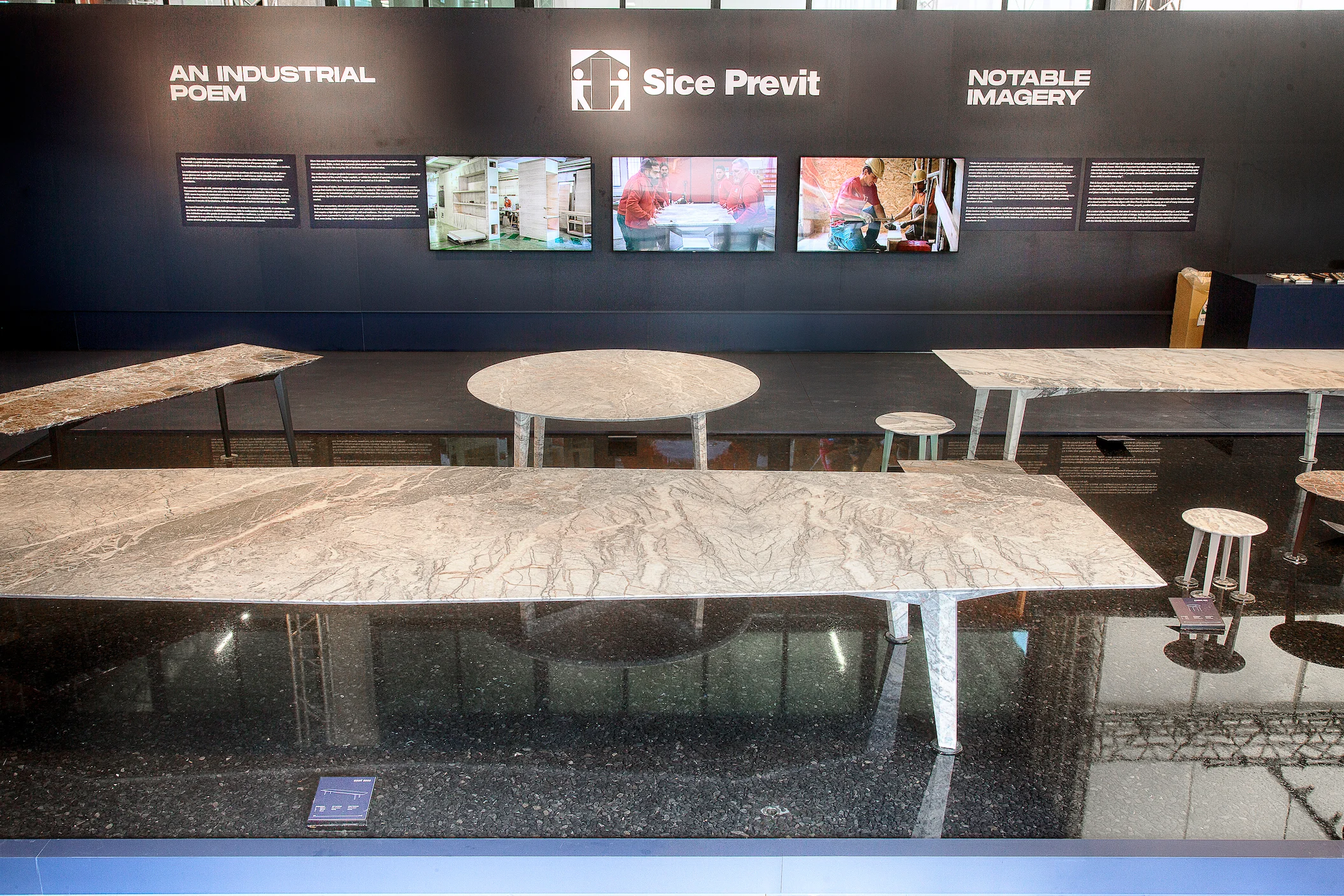 Front view of the exhibition: marble tables in a black pool facing the Sice Previt wall with screens and texts – Factory Reflections at Sice Previt, Segrate, Italy, 2024 – exhibition design