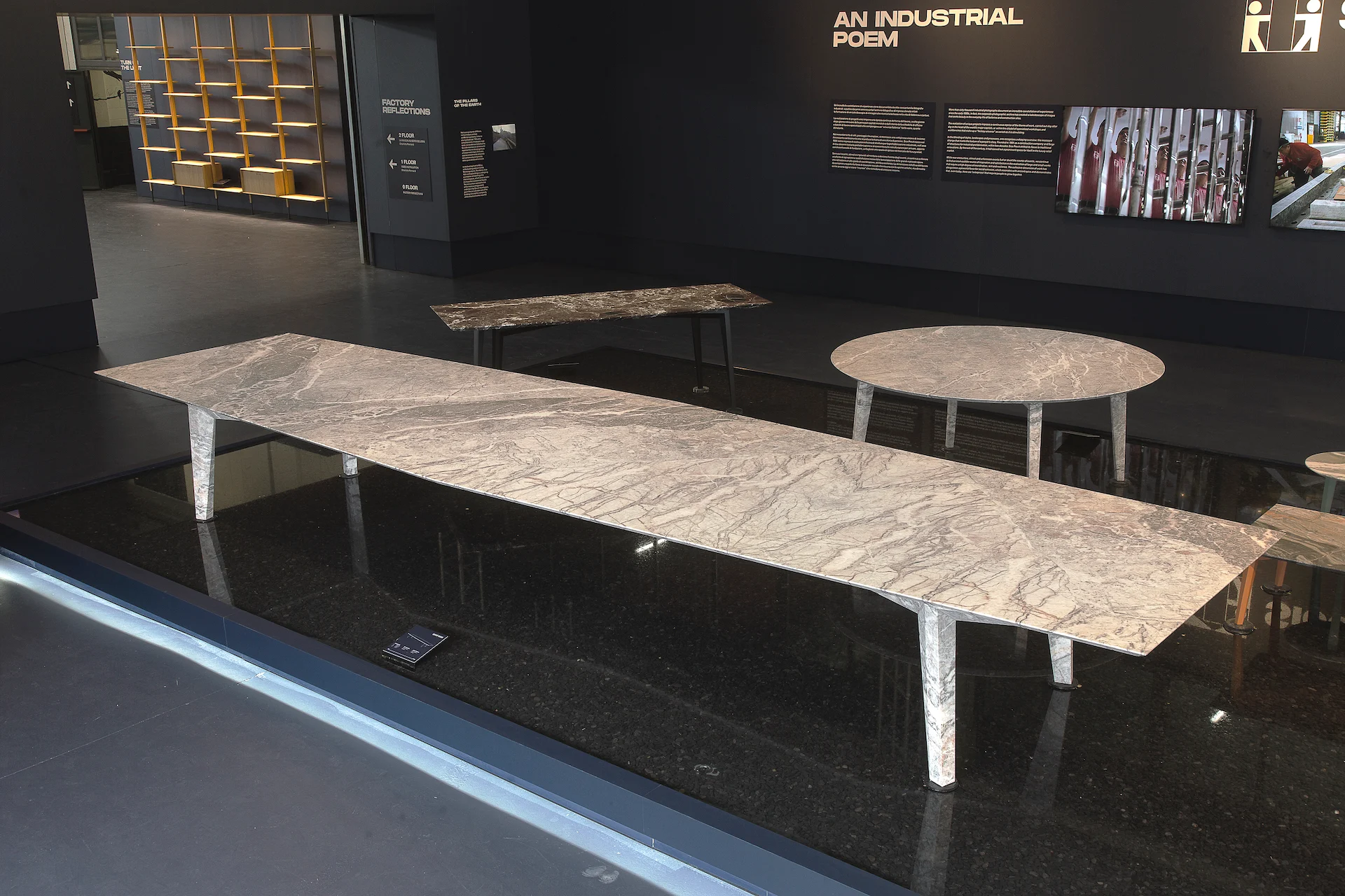Long marble table with tapered steel legs set over a black reflective floor, under the wall title An Industrial Poem – Factory Reflections at Sice Previt, Segrate, Italy, 2024 – exhibition design