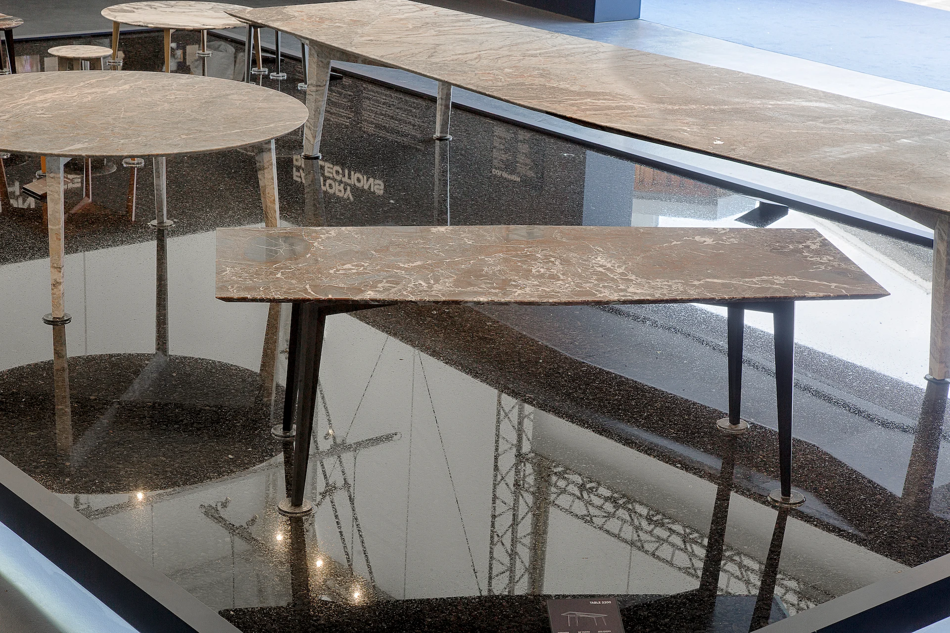 Close-up of marble tables with slender legs standing in dark water that mirrors the factory roof structure – Factory Reflections at Sice Previt, Segrate, Italy, 2024 – exhibition design