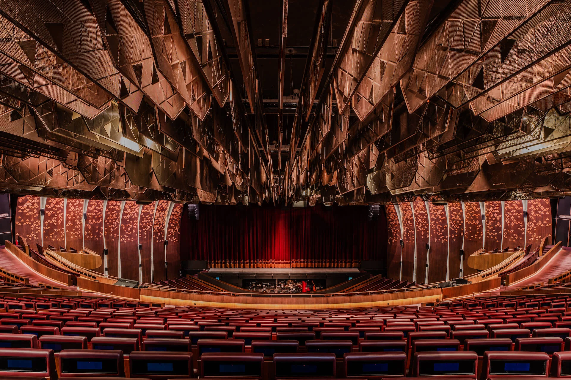Theatre auditorium from the stalls: red seats facing a red curtain beneath a ceiling of faceted copper panels – King Fahad Cultural Center, Riyadh, Saudi Arabia, 2024 – architectural renovation