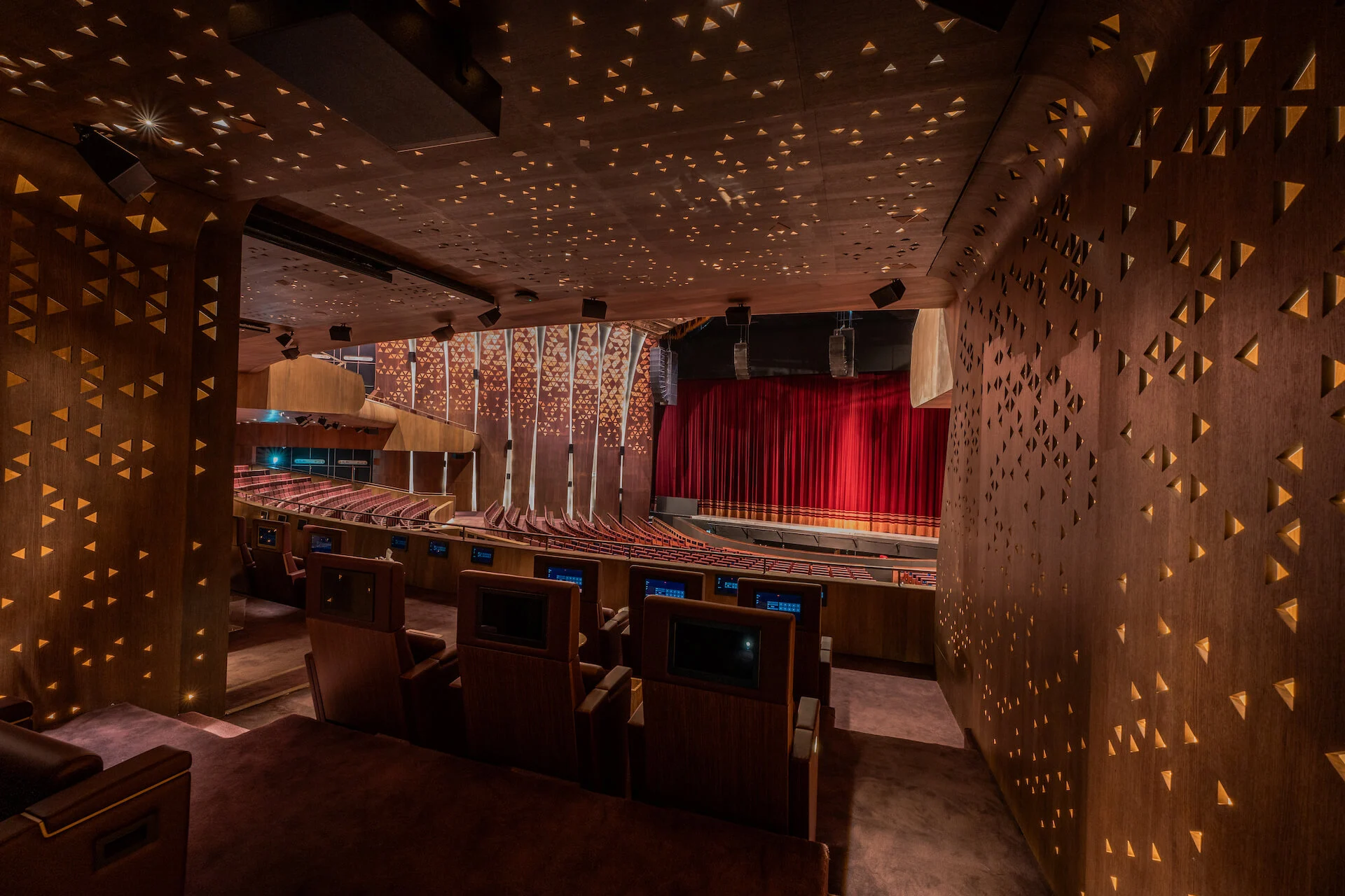 View from a box through wooden walls pierced with triangular lights towards the stage and red curtain – King Fahad Cultural Center, Riyadh, Saudi Arabia, 2024 – architectural renovation