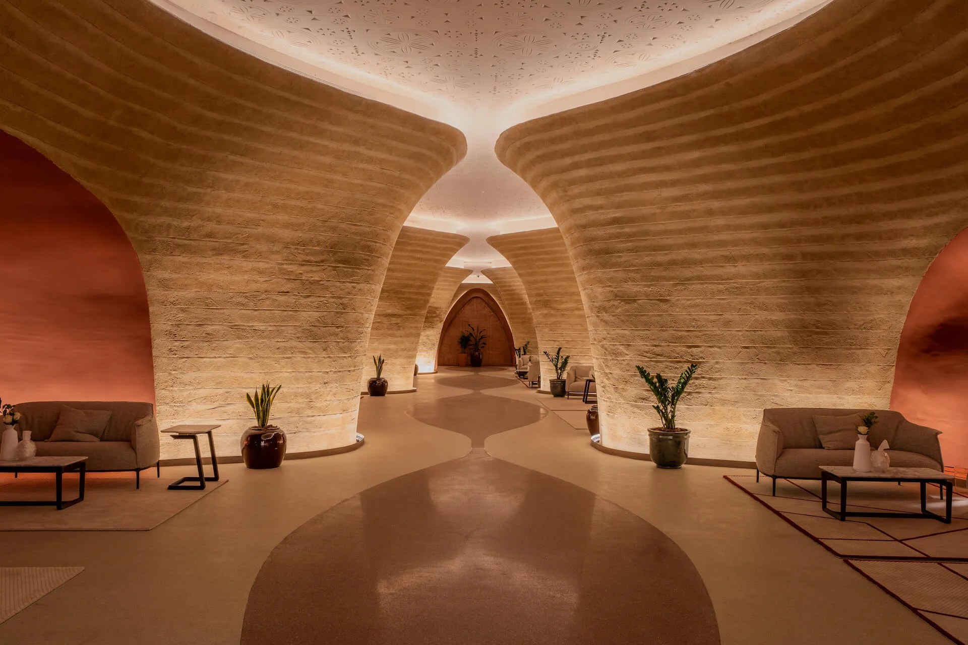 Foyer with curved rammed-earth walls, lounge sofas, potted plants and a softly lit oval ceiling – King Fahad Cultural Center, Riyadh, Saudi Arabia, 2024 – architectural renovation