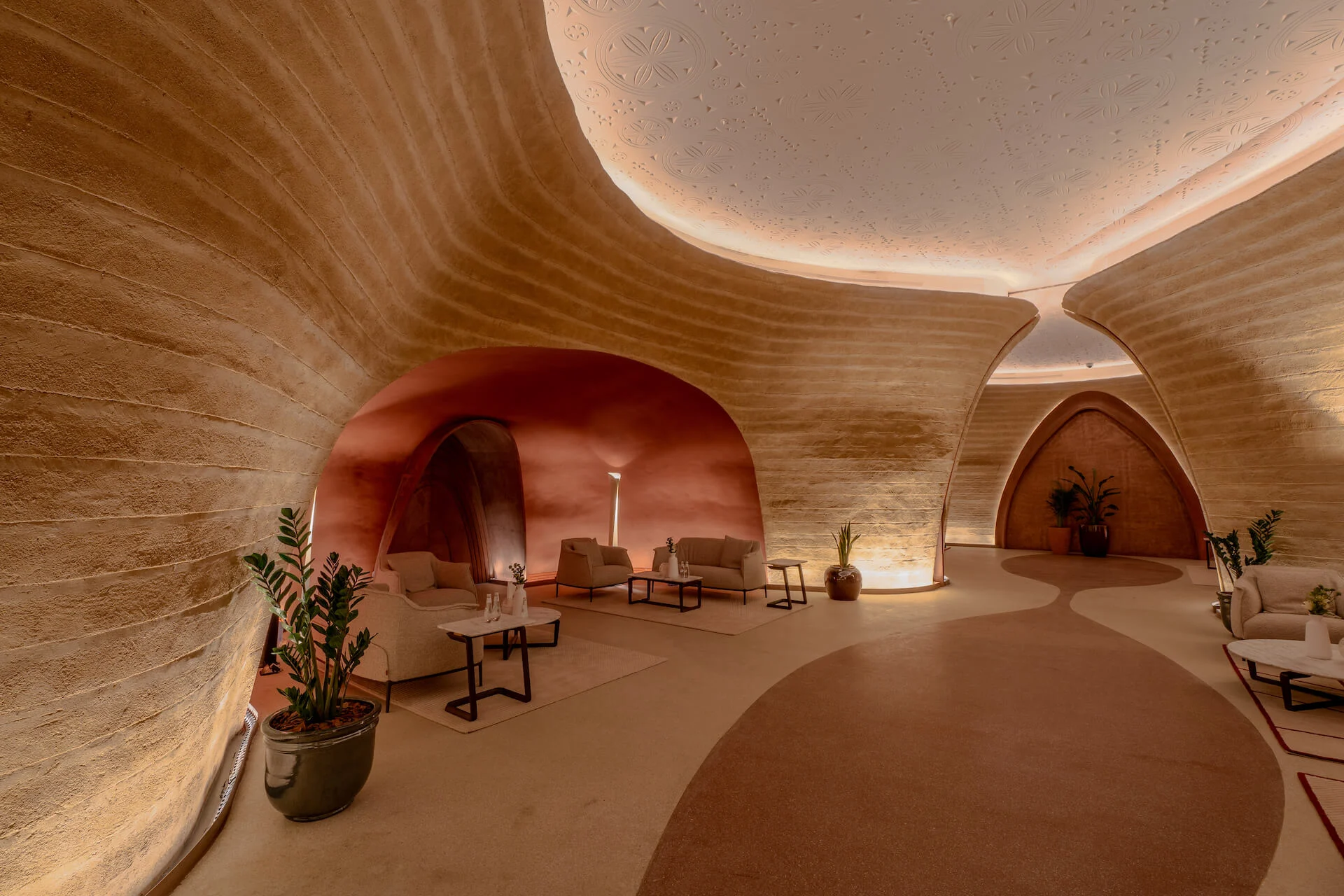 Lounge nook in a curving earthen hall, with armchairs under a terracotta vault and a winding floor pattern – King Fahad Cultural Center, Riyadh, Saudi Arabia, 2024 – architectural renovation