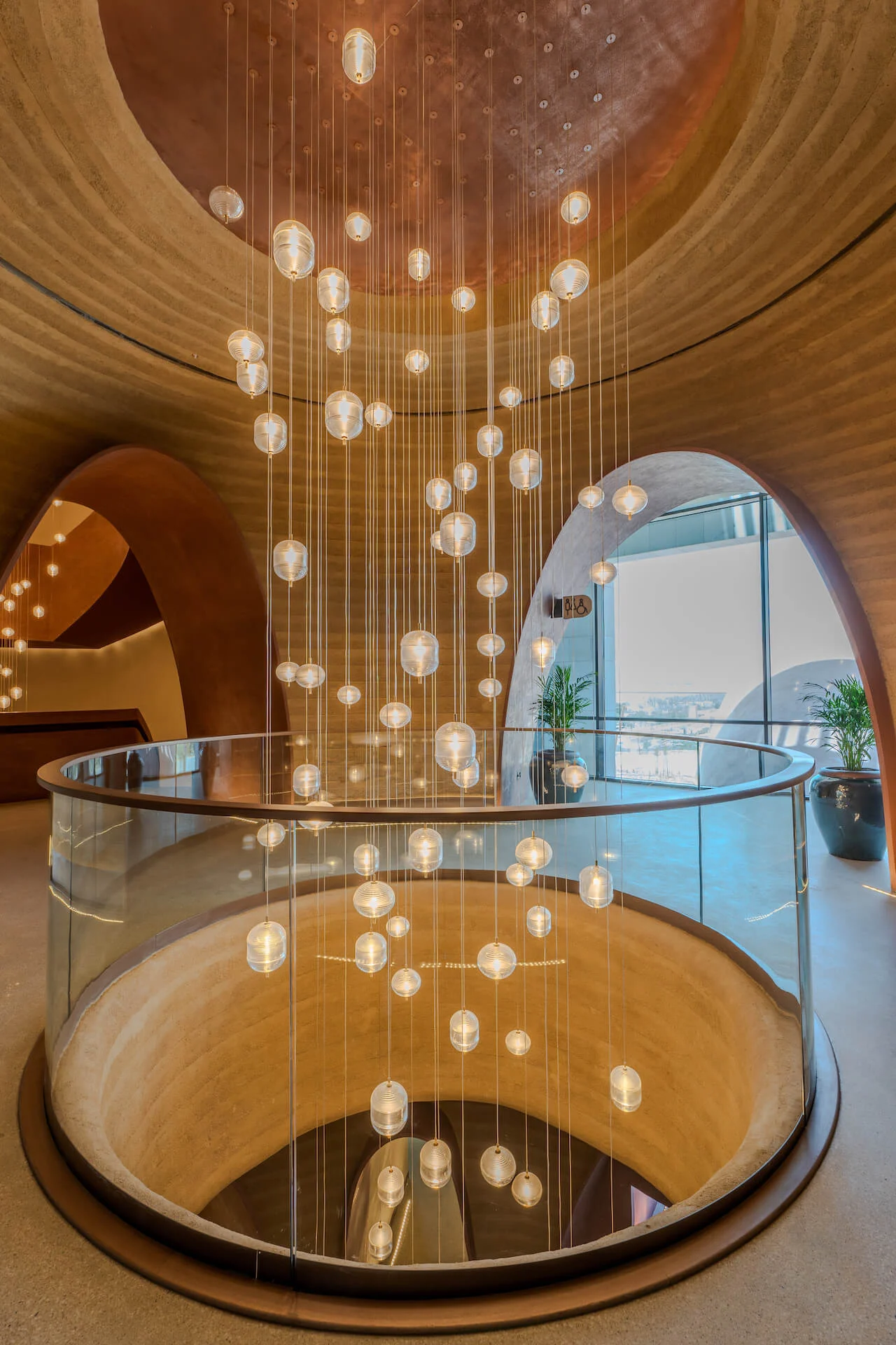 Round glass-railed stairwell with a cascade of hanging glass globe lights below a copper dome – King Fahad Cultural Center, Riyadh, Saudi Arabia, 2024 – architectural renovation