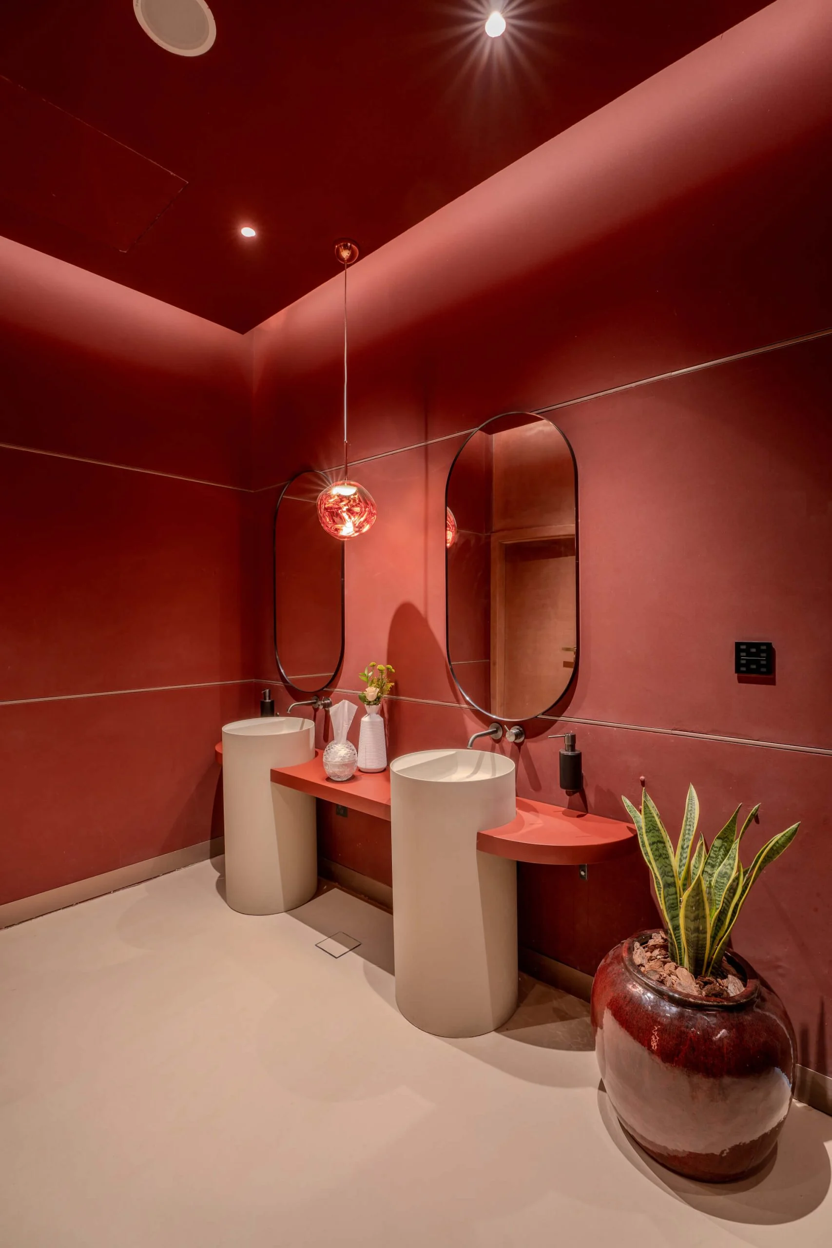 Red restroom with two white pedestal basins, oval mirrors, a pendant lamp and a large potted plant – King Fahad Cultural Center, Riyadh, Saudi Arabia, 2024 – architectural renovation