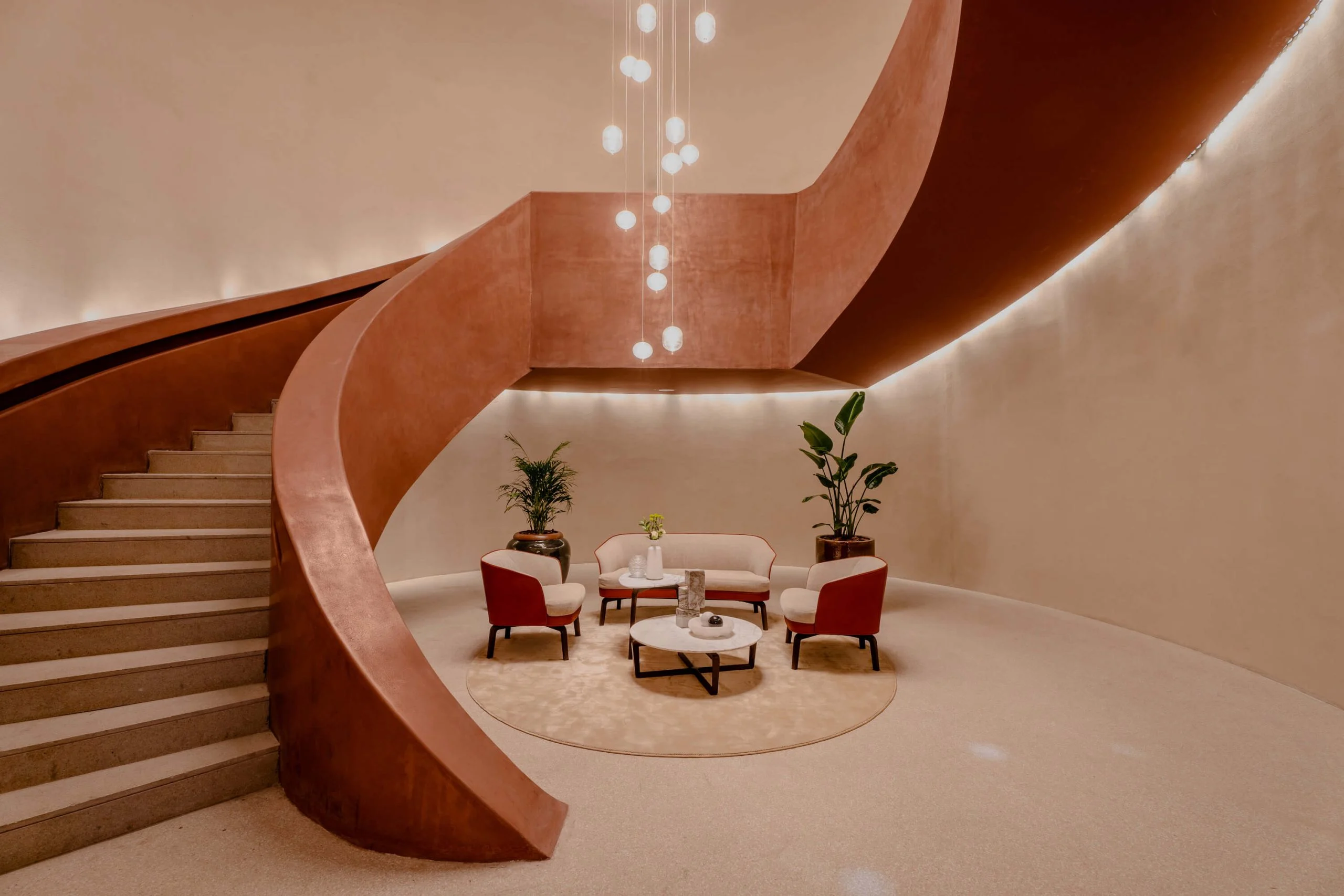 Sweeping terracotta spiral staircase around a small seating area with red armchairs and hanging lights – King Fahad Cultural Center, Riyadh, Saudi Arabia, 2024 – architectural renovation