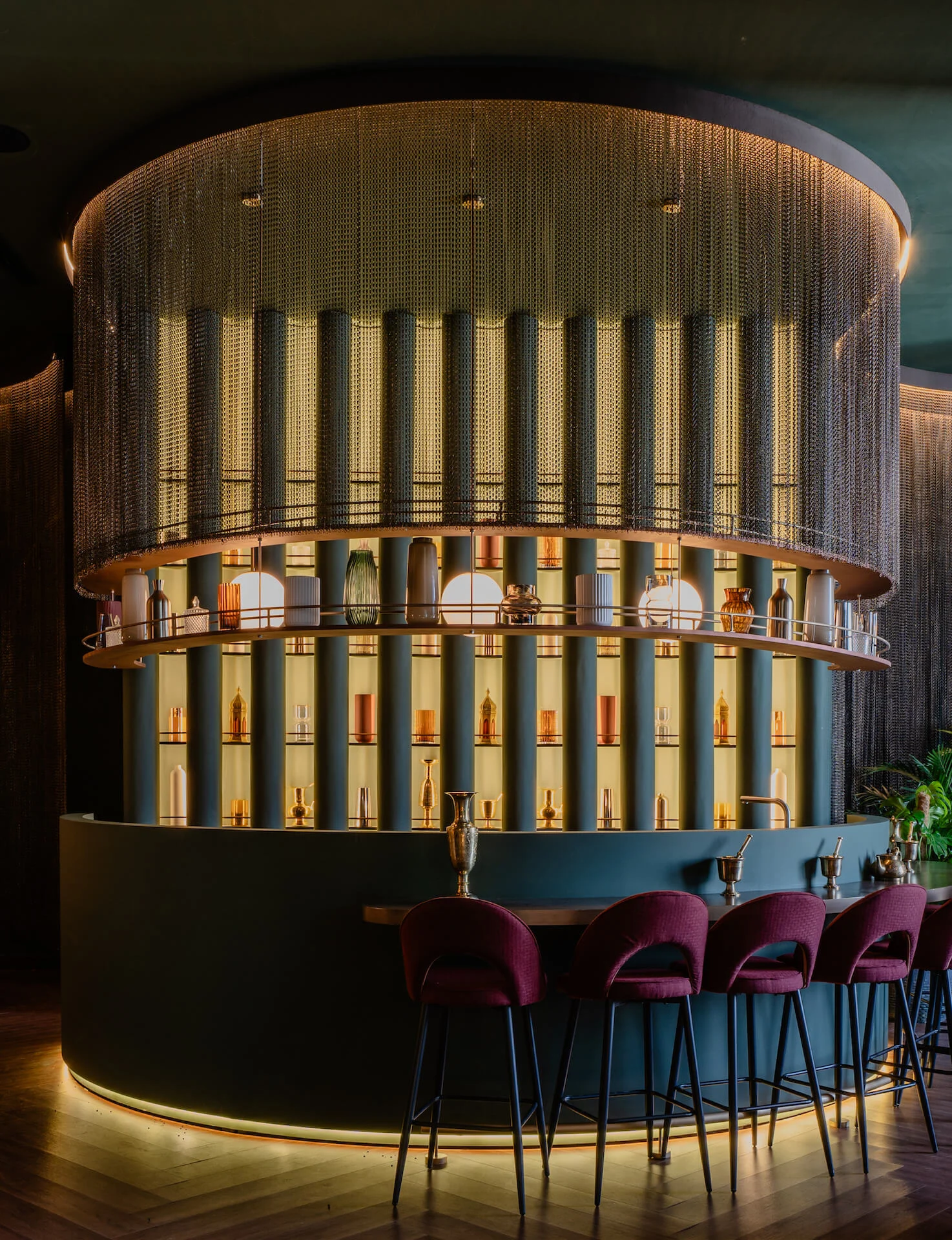 Round bar with bottles on lit shelves behind a metal chain curtain, and burgundy velvet bar stools – King Fahad Cultural Center, Riyadh, Saudi Arabia, 2024 – architectural renovation