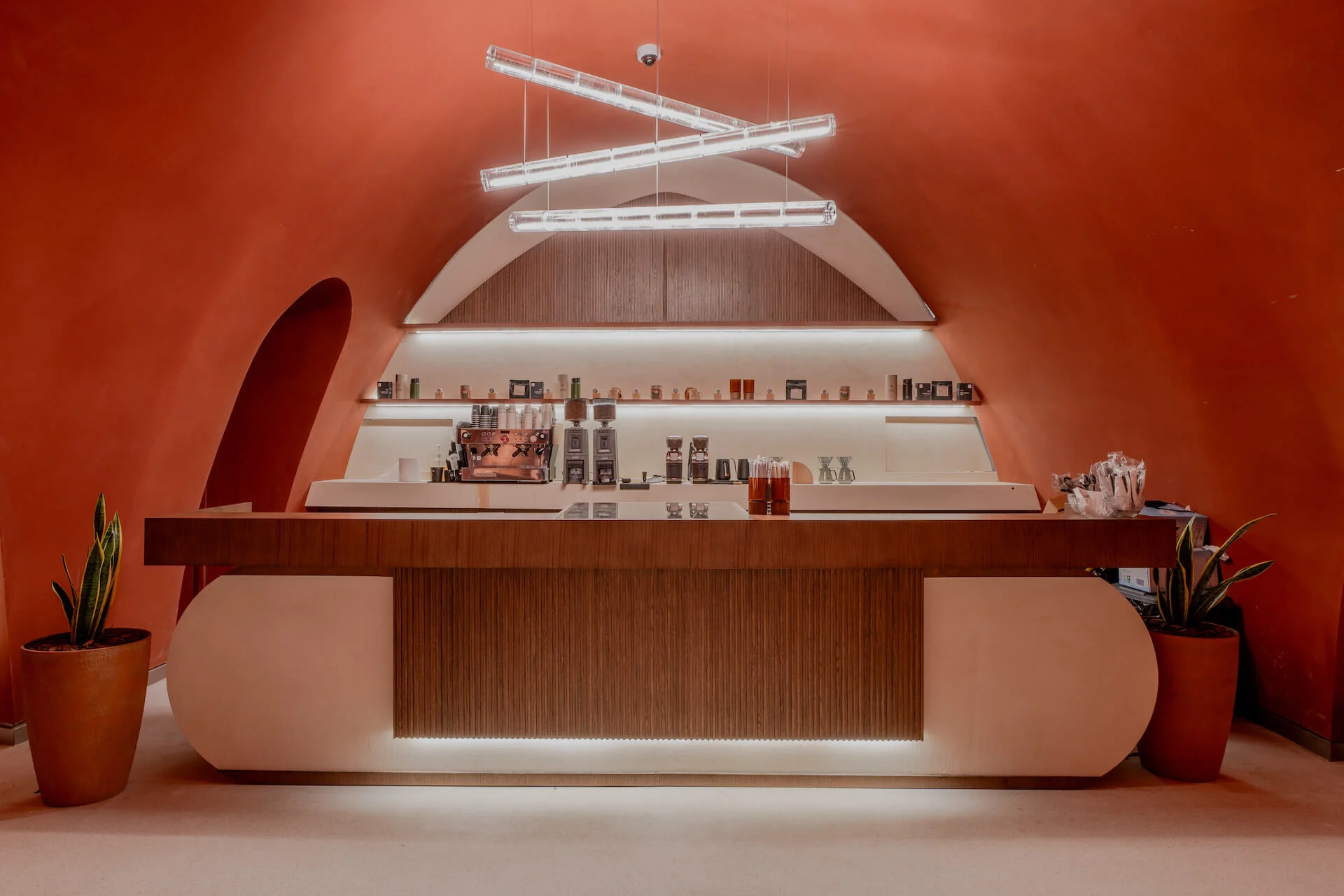 Coffee bar with a wood and white counter below suspended linear lamps, set in a terracotta arched niche – King Fahad Cultural Center, Riyadh, Saudi Arabia, 2024 – architectural renovation